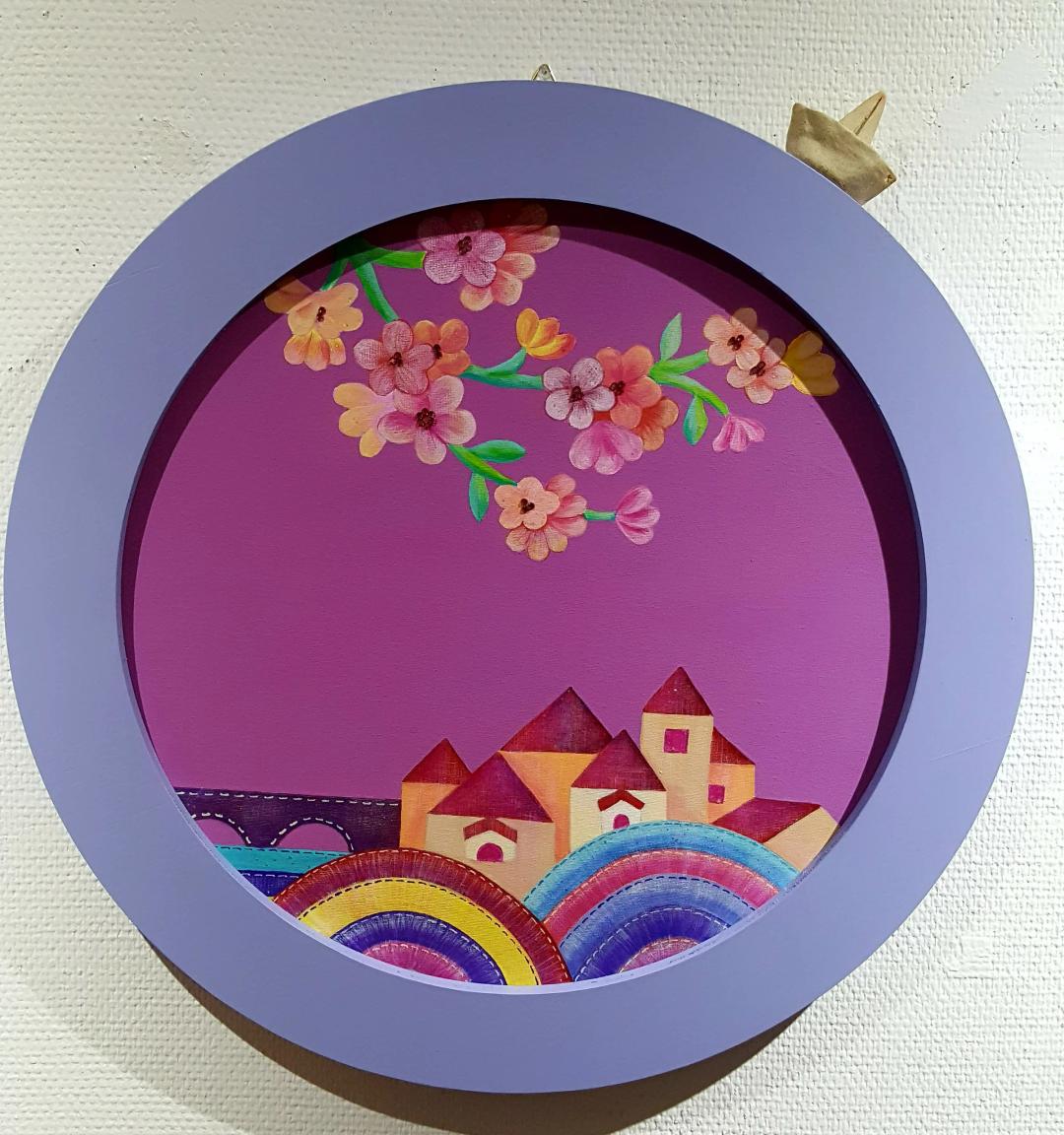 이경아, 〈꿈꾸는 종이배〉, 혼합재료, 50x50cm — 연보라 원형 틀 안에 자홍색 하늘과 꽃가지, 아래쪽 무지개 언덕 위의 작은 집들, 틀 바깥 오른쪽 위에 접은 종이배 하나